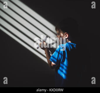 Sunlight falling on boy playing with toy airplane on wall in darkroom Stock Photo