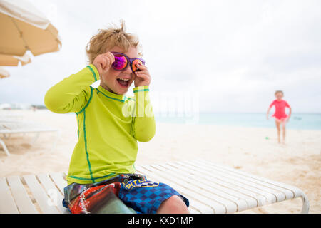 Playful boy wearing shiny sunglasses while sitting on lounge chair at beach Stock Photo