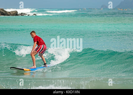 Young man learns to surf on a long board on learner waves in a paradise location. Stock Photo