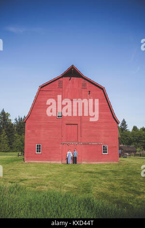 Man and woman standing on grassy field against red barn at Campbell Valley Regional Park against sky Stock Photo