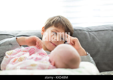 Brother looking at newborn sister on sofa at home Stock Photo