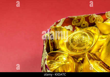 Chinese gold ingots (English translation for foreign text means blessing,rich and luck) with red pouch isolated on red background. Stock Photo