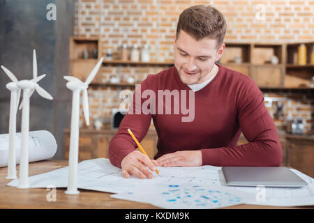 Attentive engineer smiling while drawing on the scheme Stock Photo
