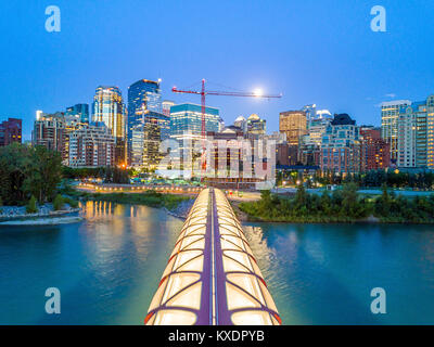 Calgary downtown at dusk with iluminated Peace Bridge and full moon, Alberta, Canada