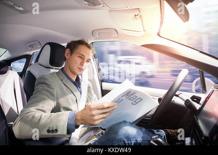 Caucasian driver reading magazine in autonomous car. Self driving vehicle. Driverless car.