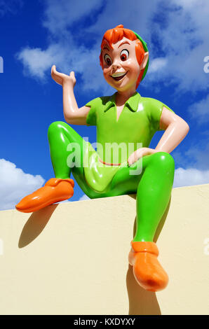 This vivid colored figure of Peter Pan  is part of a a huge private collection seen here sitting on a wall in one of his typical poses with a blue sky. Stock Photo