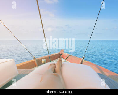 Private boat trip on open sea. Image shows legs of a woman lying on a thick and comfortable cushion laid on top of boat. which is sailing in a beautif Stock Photo
