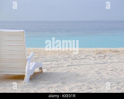 White plastic beach chair on a white sand beach with baby black-naped tern or sterna sumatrana on the right side.The bird belongs to Laridae family Stock Photo