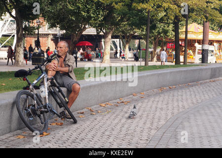 Man resting and crowd watching on a low wall with his push bike, near the London Eye Stock Photo