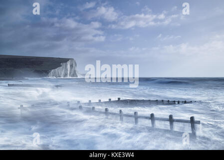 Stormy sea crashing over sea defences in front of white cliffs at Cuckmere Haven. Stock Photo