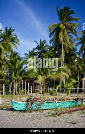 Depth of field shot of a basic Filipino pump boat on the shore of a white sand beach with a back ground of fenced area, palm trees and a basic bamboo  Stock Photo