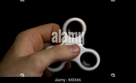 Male hand with white spinner isolated on black background. White fidget spinner device on black background. Playing with a white hand spinner fidget toy. White spinner in man hand on black background Stock Photo