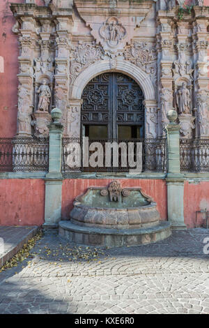 Beautiful arched entrance to the Templo de San Francisco with cobblestone street, iron railing, pink walls and stone fountain, in Guanajuato, Mexico Stock Photo