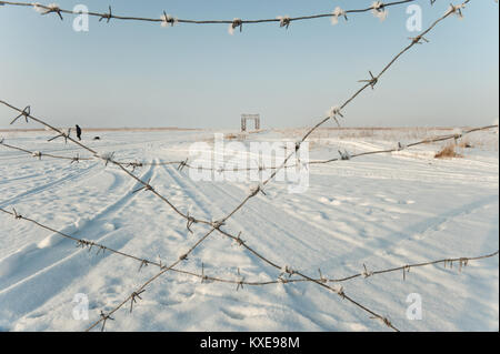 Barbed wire on a background of snow-covered landscape in sunny winter day Stock Photo