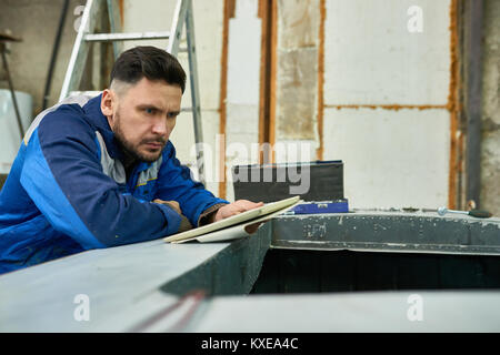 Portrait of handsome bearded worker using digital tablet while  repairing boat in yacht workshop, copy space Stock Photo
