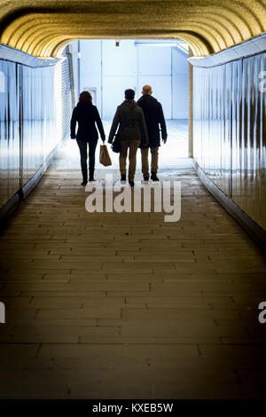 Three people are silhouetted as they walk through a tunnel Stock Photo