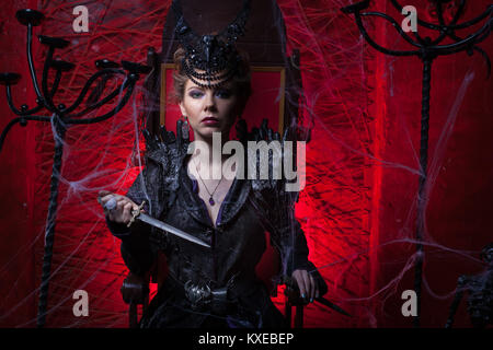 Woman in black dress sitting on a throne and holding a dagger. Stock Photo