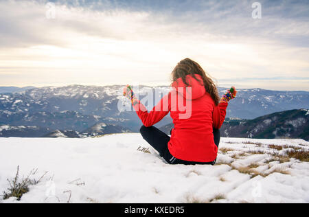 Girl meditating on snow covered mountain top at sunset Stock Photo
