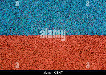 Red and blue color synthetic rubber running track granules textured background separated through the middle. Stock Photo