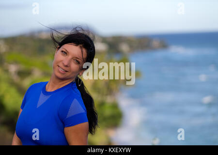 Happy young woman with her hair blowing in the wind looking at the camera with a smile as she poses on Diamond head, Oahu, Hawaii Stock Photo