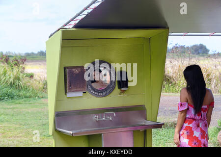 Young woman using an open air restroom in Oahu, Hawaii reflected in the mirror hanging on the wall Stock Photo