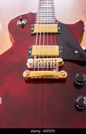 Shiny Wine Red Guitar With Golden Hardware on A Wooden Table With Focus on the Stop Bar Stock Photo