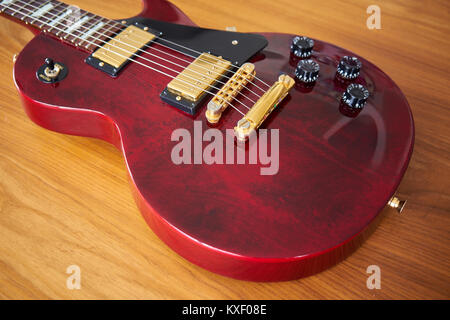 Shiny Wine Red Guitar With Golden Hardware on A Wooden Table Side Angled View Stock Photo