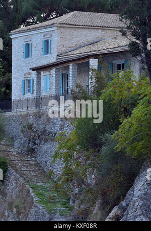 A typically Greek house on rocks raised above the shoreline on the beach at Agni on the island of Corfu in greece. Steps leading up rocks to a house. Stock Photo