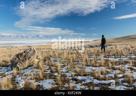 A man admires a stunning view of the snow-covered Wasatch Mountains from Antelope Island State Park in winter. Stock Photo