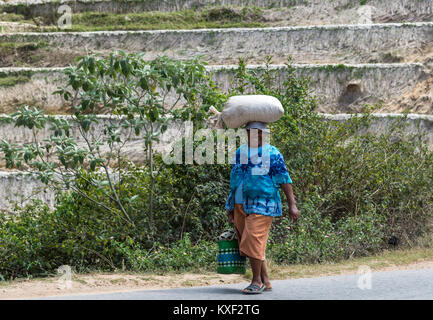 A local woman with a big smile carrying a sack over her head. Madagascar, Africa. Stock Photo