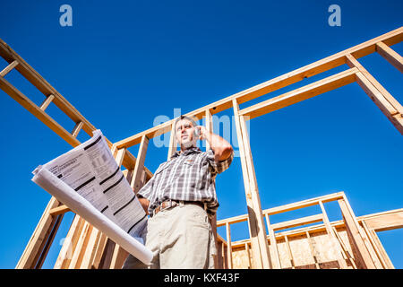 A young professional man on his cell phone while looking at plans in a residential contruction site. Stock Photo
