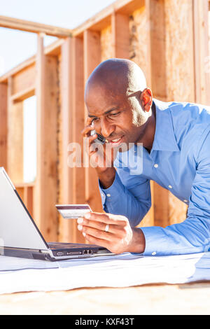 A man on his phone looking at a laptop computer and using his credit card. Stock Photo