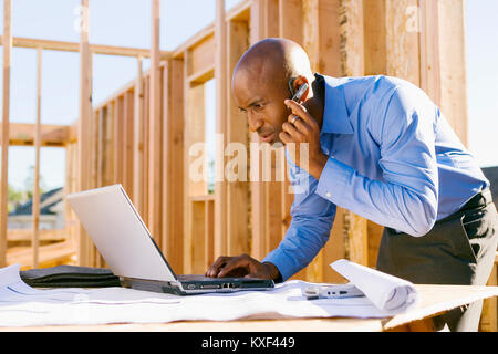 A man on his wireless bluetooth headset looking at a laptop computer. Stock Photo