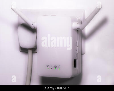 Netgear wifi / wi-fi wireless internet extender, with twin antennas plugged into an electrical wall socket, with activity lights glowing. England, UK. Stock Photo