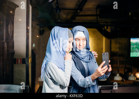 two happy young muslim woman take self portrait with handphone at cafe Stock Photo