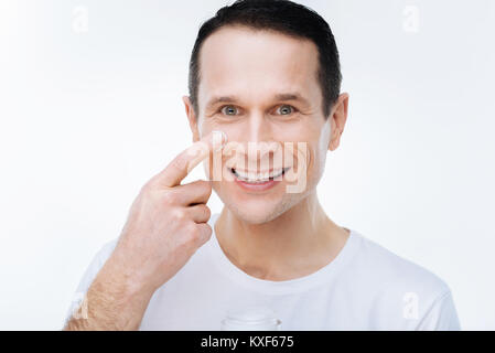 Portrait of a delighted nice man putting on facial cream Stock Photo