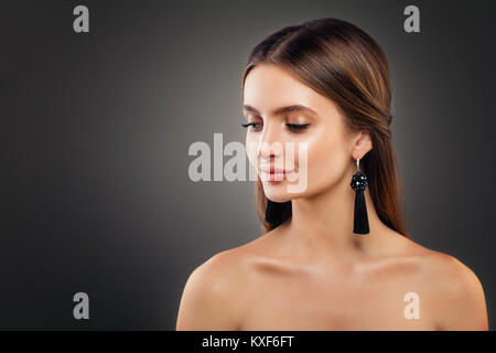 Stylish Young Woman Fashion Model with Shiny Makeup and Black Silky Jewelry Earrings on Background with Copy space Stock Photo