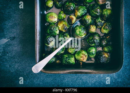 Brassica oleracea. Roasted Brussel sprouts in a baking tray with spoon on a slate background. Vintage filter applied Stock Photo