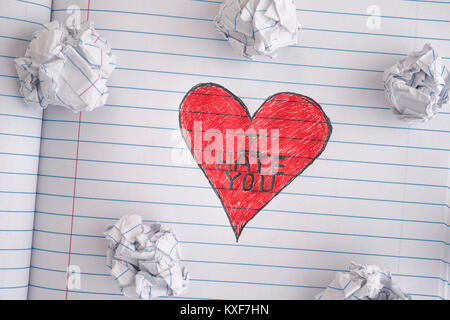 I Hate You. Red Heart with phrase I Hate You on notebook sheet with some crumpled paper balls on it. Close up. Stock Photo