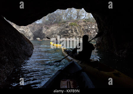 Sea kayakers in abalone diving wetsuits paddle through a sea cave near Russian Gulch State Park. Stock Photo