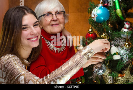 happy family at new year. senior grandma and young caucasian woman decorating christmas tree. old grandmother and granddaughter, teen, teenager. Stock Photo