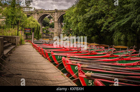 The riverside at Knaresborough North Yorkshire. Many red rowing boats are moored on the bank of the river Nidd in the background is the train bridge Stock Photo