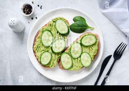 Toasts with mashed avocado and cucumber on white plate. Top view. Healthy eating, dieting, cleansing concept Stock Photo