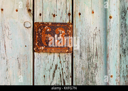 Rusty grunge metal house number plaque No. 63 on an old wooden door, vintage signs in Greece. Stock Photo
