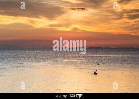 Kayakers paddle across the calm sea under a saturated sunset sky in Anilao, Philippines. Stock Photo