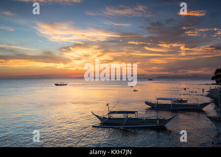 Bangka boats rest on the shoreline under a vibrant sunset sky in Anilao, Philippines. Stock Photo