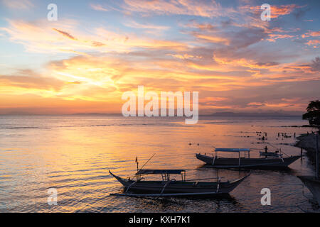 Bangka boats rest on the shoreline under a vibrant sunset sky in Anilao, Philippines. Stock Photo