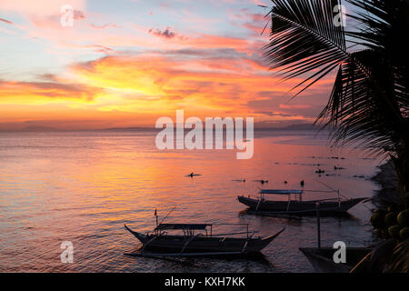 Bangka boats rest on the shoreline under a vibrant sunset sky in Anilao, Philippines. Stock Photo