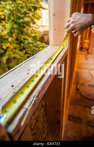 A mans hands measuring a window opening in a house under construction. Stock Photo