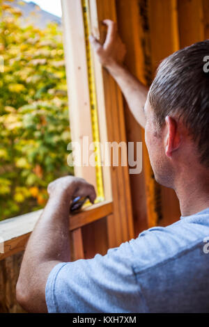 A man measuring the inside of a window frame on a residential house under construction. Stock Photo